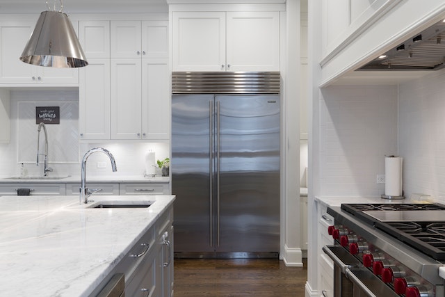 A modern kitchen in a rental with stainless steel appliances white marble countertops white cabinets and a large center island